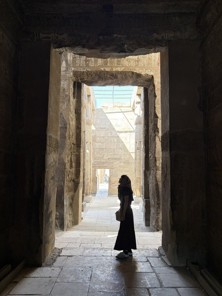 古代神殿の柱廊で光を見上げる、肌の露出を抑えたロング丈の服装（2026年5月撮影）